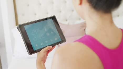 Asian-woman-using-tablet-with-smart-home-interface-in-bedroom,-in-slow-motion