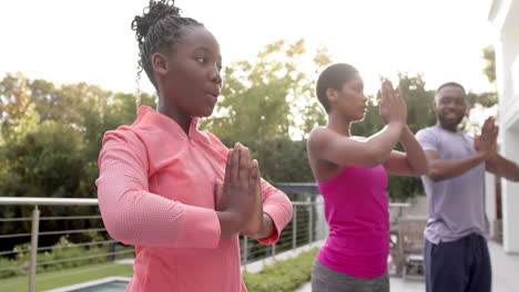 Felices-Padres-Afroamericanos-E-Hija-Practicando-Yoga-En-Un-Jardín-Soleado,-En-Cámara-Lenta