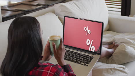 Biracial-woman-using-laptop-on-couch-at-home-online-shopping-during-sale,-slow-motion