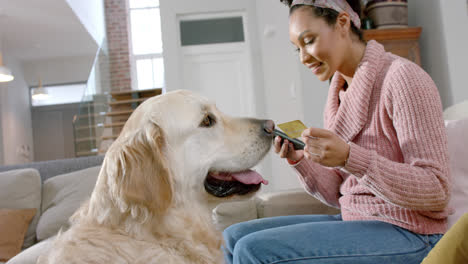 Happy-biracial-woman-with-golden-retriever-dog-using-smartphone-and-credit-card-at-home,-slow-motion