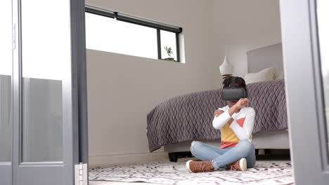 African-american-boy-sitting-on-floor-using-vr-headset-in-bedroom-at-home,-slow-motion,-copy-space