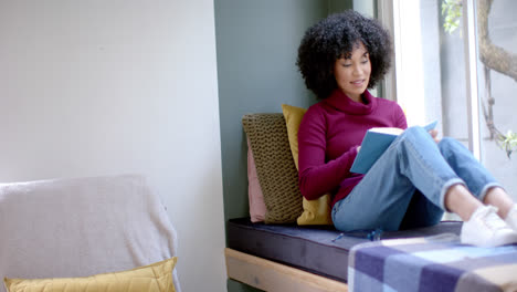 Happy-biracial-woman-reading-book-at-home,-slow-motion,-copy-space