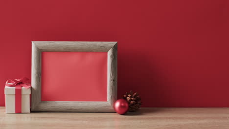 Video-of-christmas-decorations-and-wooden-frame-with-copy-space-on-red-background