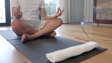 Midsection-of-biracial-man-doing-yoga-and-meditating-at-home,-slow-motion