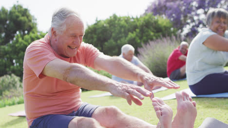 Happy-caucasian-man-touching-toes-with-diverse-group-of-seniors-exercising-in-garden,-slow-motion