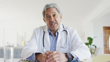 Senior-biracial-male-doctor-talking-and-gesturing-during-video-consultation