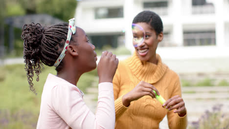 Happy-african-american-mother-and-daughter-blowing-bubbles-in-sunny-garden