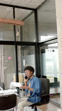 Vertical-video-of-african-american-man-using-smartphone-and-holding-documents-at-home,-slow-motion