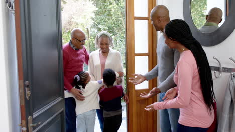 Happy-african-american-parents,-son-and-daughter-welcoming-grandparents-at-front-door,-slow-motion