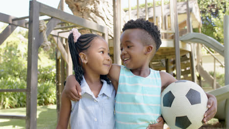 Portrait-of-happy-african-american-siblings-with-football-in-garden,-in-slow-motion