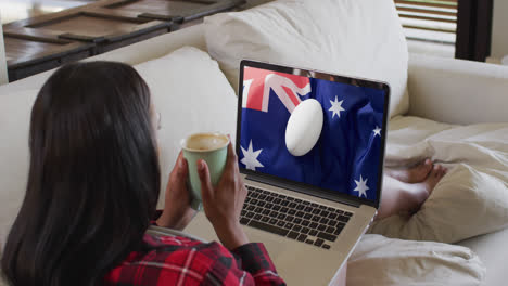 Mujer-Birracial-Mirando-Una-Computadora-Portátil-Con-Una-Pelota-De-Rugby-En-La-Bandera-De-Australia-En-La-Pantalla