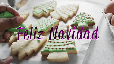 Feliz-navidad-text-in-purple-over-african-american-hand-decorating-christmas-cookies