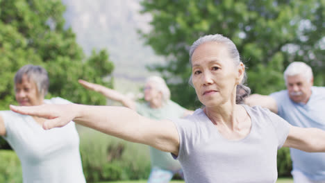 Lächelnde-ältere-Asiatische-Frau,-Die-Yoga-Mit-Einer-Vielfältigen-Seniorengruppe-Im-Garten-Praktiziert,-Zeitlupe