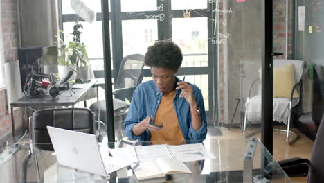 Afroamerikanischer-Gelegenheitsgeschäftsmann,-Der-Zu-Hause-Mit-Smartphone-Und-Laptop-Am-Schreibtisch-Sitzt,-Zeitlupe
