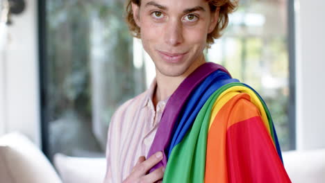 Porträt-Eines-Glücklichen-Kaukasischen-Mannes-Mit-Regenbogen-LGBT-Flagge-Zu-Hause,-Zeitlupe