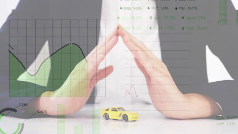 Animation-of-data-processing-on-graphs-over-caucasian-woman-sheltering-toy-car-with-hands
