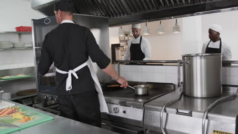 Focused-diverse-male-chef-instructing-trainee-male-chefs-in-kitchen,-slow-motion