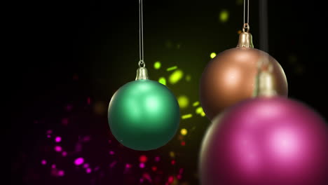 Swinging-colourful-christmas-baubles-over-colourful-dancing-lights-on-black-background
