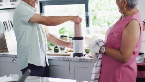 Happy-senior-biracial-couple-preparing-healthy-drink-in-kitchen