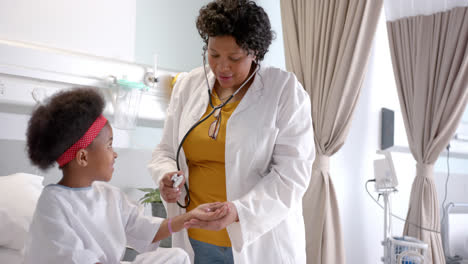 African-american-female-doctor-examining-girl-using-stethoscope-in-hospital-room,-slow-motion