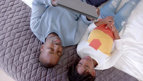 Happy-african-american-father-and-son-lying-on-bed-using-tablet-at-home,-slow-motion