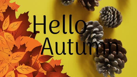 Animation-of-hello-autumn-text-over-pine-cones-and-autumn-leaves-on-yellow-background