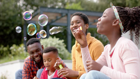Felices-Padres-Afroamericanos,-Hijo-E-Hija-Soplando-Burbujas-En-Un-Jardín-Soleado