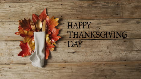 Animation-of-happy-thanksgiving-text-over-cutlery-and-autumn-leaves-over-wooden-background