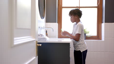 African-american-boy-brushing-teeth-in-bathroom-at-home,-slow-motion