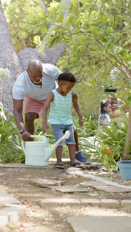 Vertical-video-of-happy-african-american-grandfather-and-grandson-gardening,-in-slow-motion