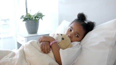 African-american-girl-lying-in-hospital-bed-and-holding-mascot,-slow-motion