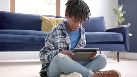 Niño-Afroamericano-Usando-Tableta-Sentada-En-El-Suelo-En-Casa,-Cámara-Lenta