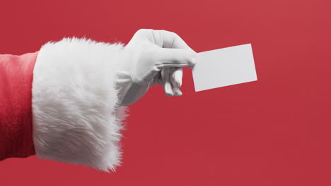 Video-of-santa-claus-holding-white-card-with-copy-space-on-red-background