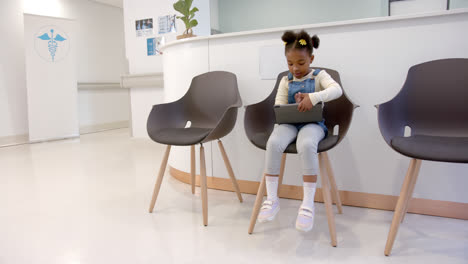Afroamerikanisches-Mädchen-Sitzt-Im-Wartezimmer-Des-Krankenhauses-Und-Benutzt-Tablet,-Zeitlupe
