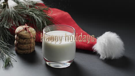 Happy-holidays-text-over-christmas-hat,-cookies-and-milk-on-dark-grey-background