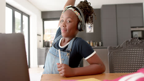 Fröhliches-Afroamerikanisches-Mädchen-Mit-Kopfhörern-Und-Laptop,-Das-Im-Online-Unterricht-Die-Hand-Hebt,-Langsame-Bewegung