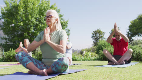 Diverse-group-of-male-and-female-seniors-practicing-yoga-meditation-sitting-in-garden,-slow-motion