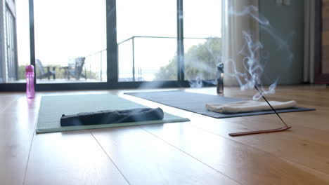 Close-up-of-yoga-mats,-water-bottles-and-incense-on-floor,-slow-motion