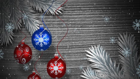 Animation-of-snow-falling-over-hanging-bauble-decorations-against-wooden-grey-background
