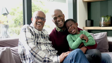 Happy-african-american-father,-son-and-grandfather-sitting-on-couch-together-laughing,-slow-motion