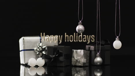 Happy-holidays-text-over-christmas-presents-and-baubles-hanging-on-dark-background