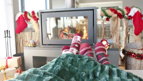 Feet-of-diverse-gay-male-couple-on-sofa-by-fireplace-at-home-at-christmas,-slow-motion