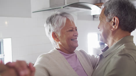 Happy-senior-biracial-couple-dancing-in-kitchen
