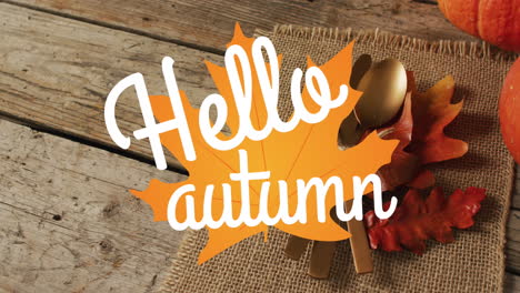 Animation-of-hello-autumn-text-over-cutlery-and-autumn-leaves-over-wooden-background