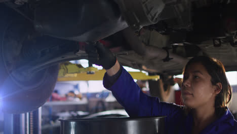 Animation-of-mid-adult-female-asian-mechanic-draining-engine-oil-from-car-in-garage