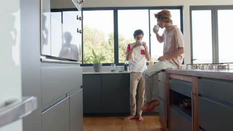 Happy-diverse-gay-male-couple-drinking-coffee-in-kitchen-at-home,-slow-motion,-copy-space