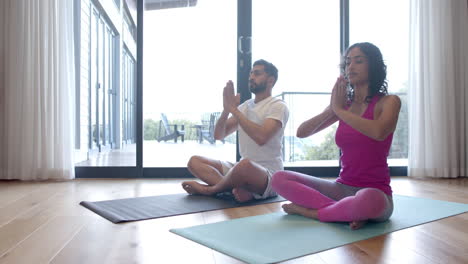 Biracial-couple-doing-yoga-and-meditating-at-home,-in-slow-motion