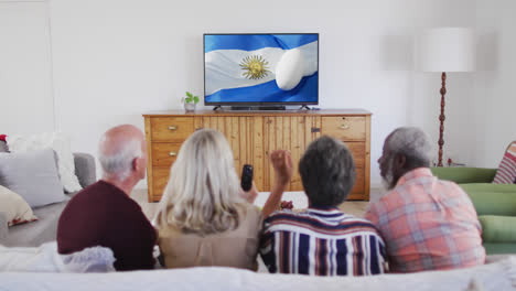 Diverse-senior-friends-watching-tv-with-rugby-ball-on-flag-of-argentina-on-screen