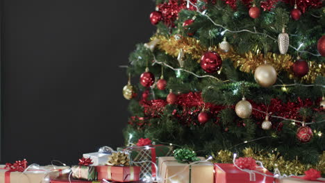 Video-of-christmas-tree-with-presents,-baubles-decorations-and-copy-space-on-black-background