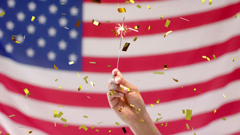 Animation-of-confetti-falling-over-hand-holding-sparkler-and-flag-of-united-states-of-america